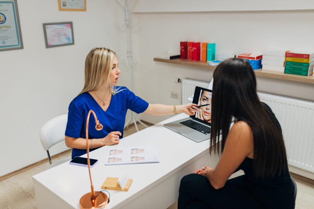 Dermatologist and beautician, explaining to the young female patient the procedure of mesotherapy treatment and dermal fillers, at her modern medical clinic