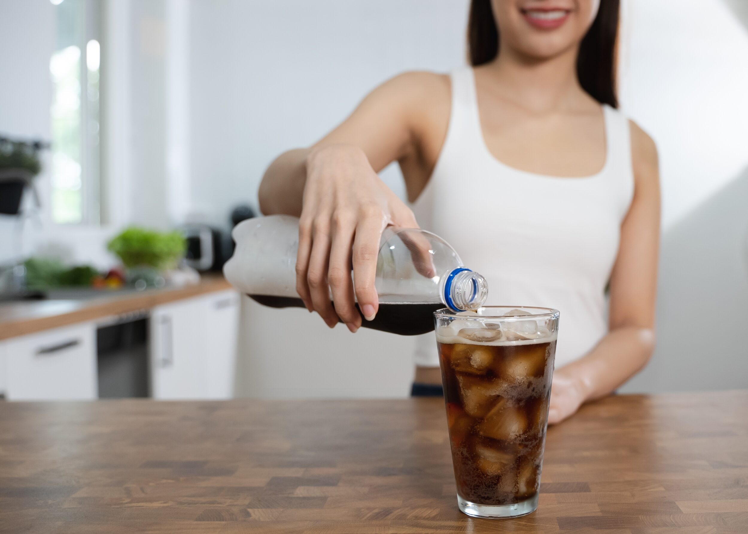 Pouring soda into glass with ice, representing sugary drink consumption